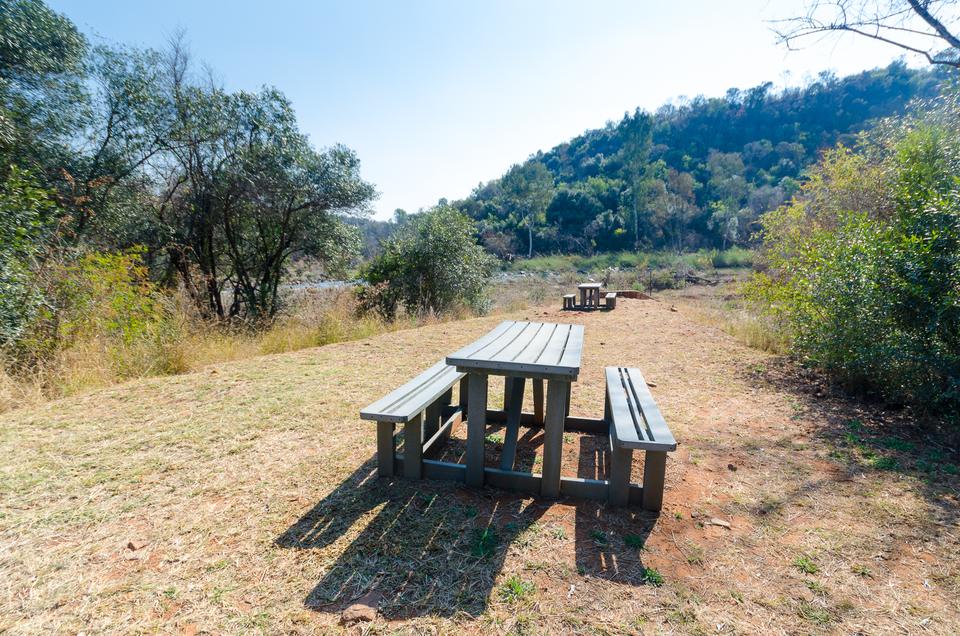 A wooden picnic table on a grassy clearing, with bushveld hills behind.