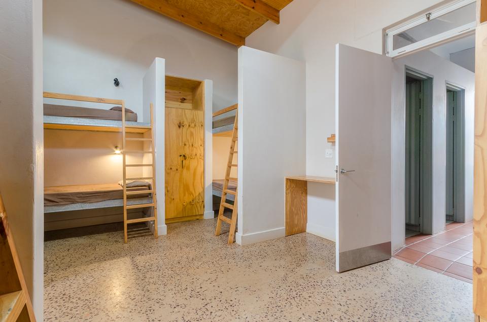A shared dorm with wooden bunk beds and a built-in desk.